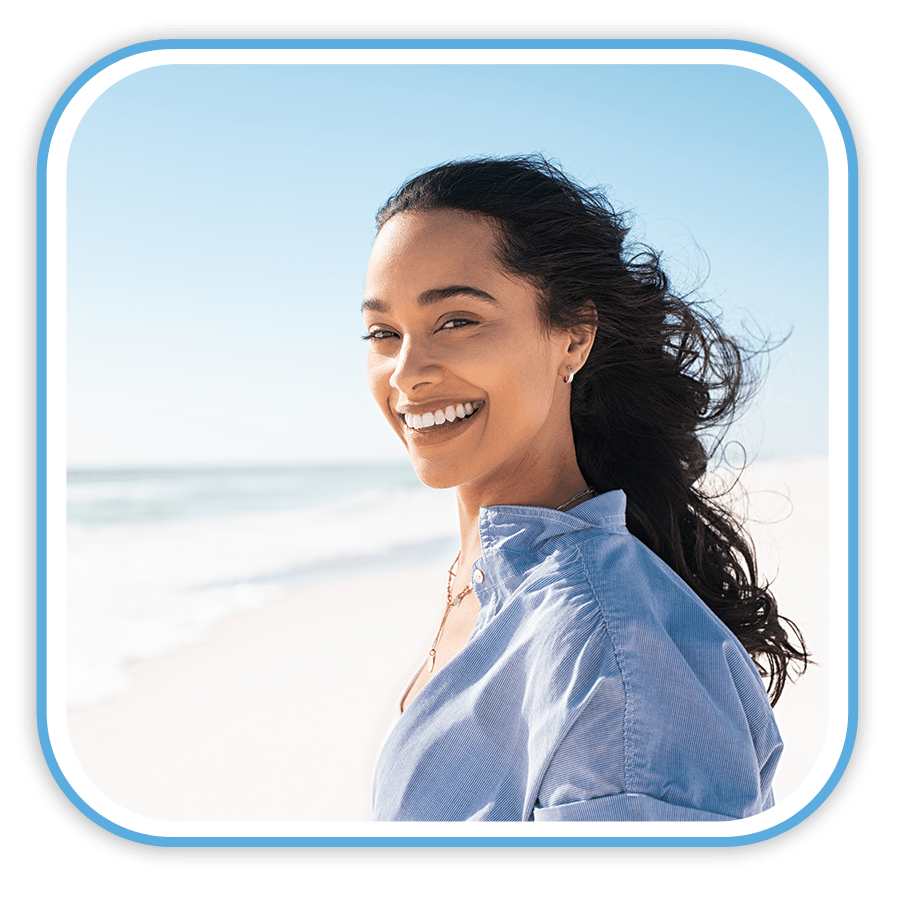 Smiling woman in blue shirt at beach, enjoying outdoor wellness and healthy lifestyle.