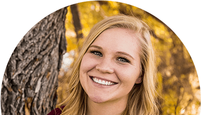 Smiling blonde woman outdoors with fall foliage background in portrait style photo.