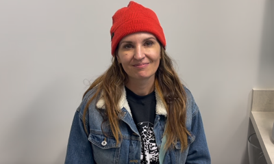Woman wearing red beanie and denim jacket smiles at camera in clinical office setting.