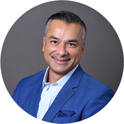 Professional headshot of male dentist in blue blazer against gray background.