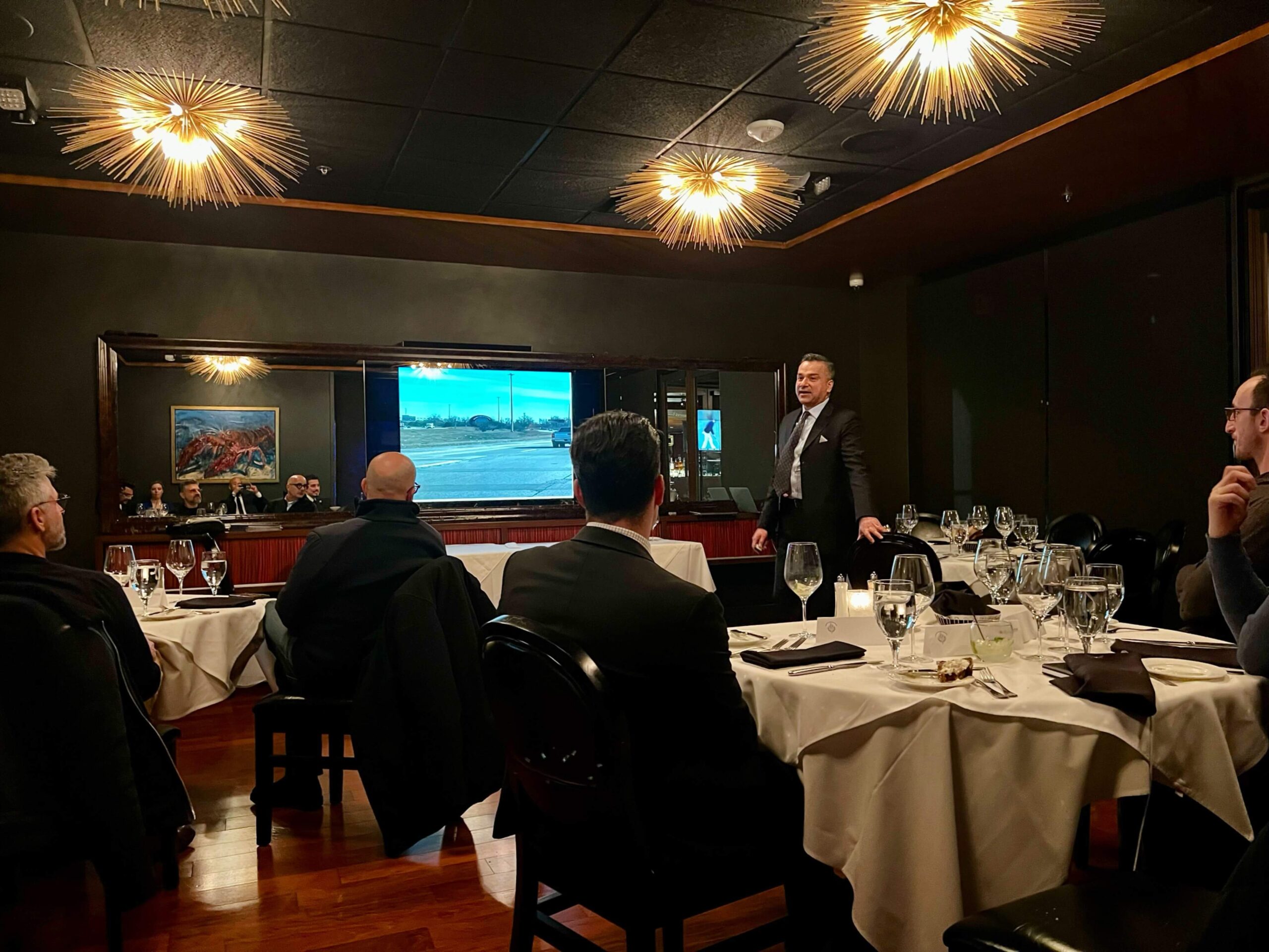 Dental professionals gather at formal banquet dinner with presentation screen displaying content.