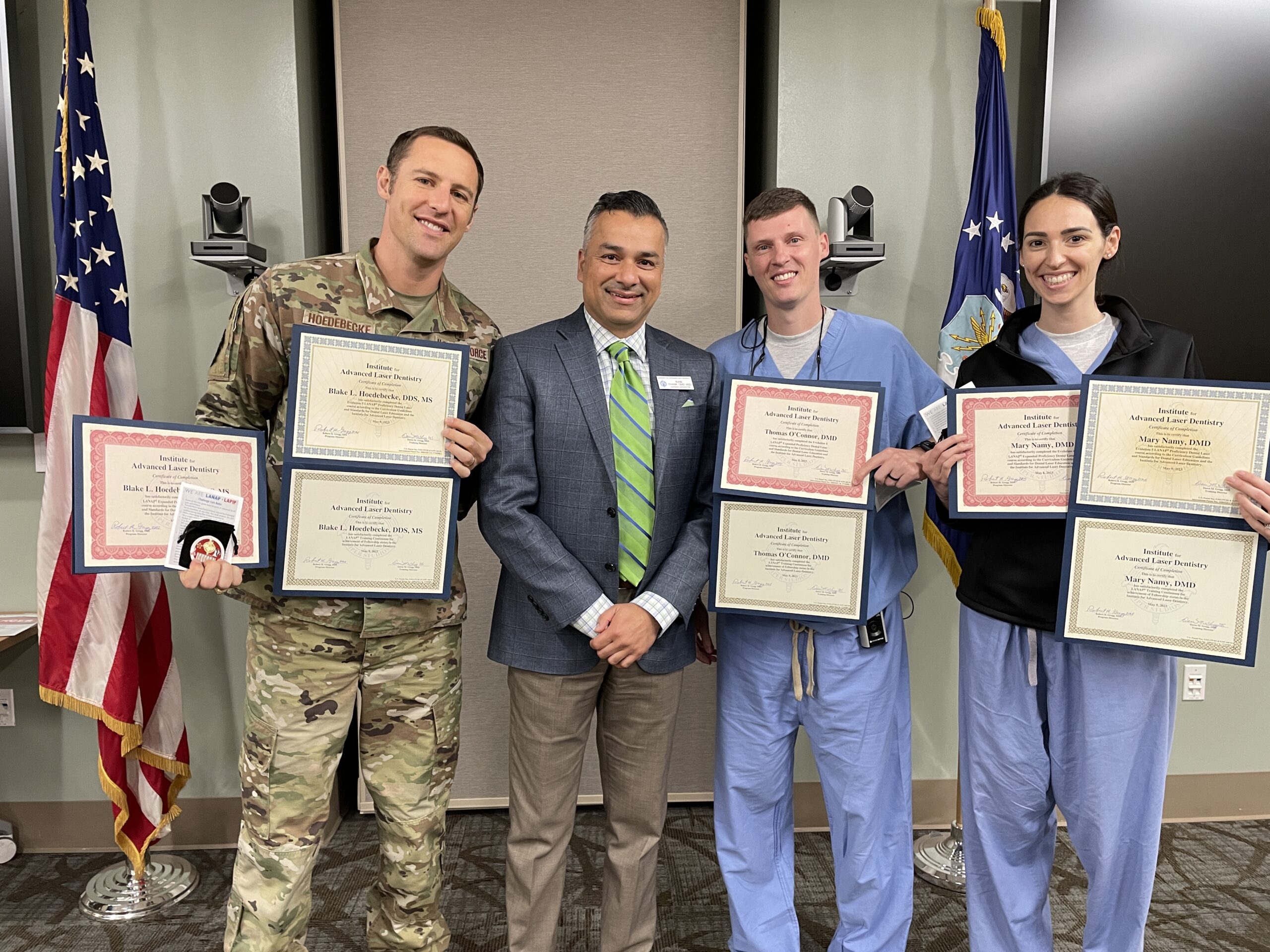 Five men holding certificates at an awards ceremony with American flags in background.