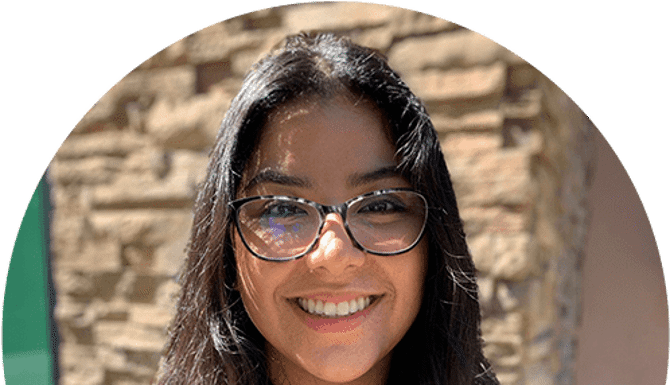 Woman wearing glasses smiling at camera against brick wall background
