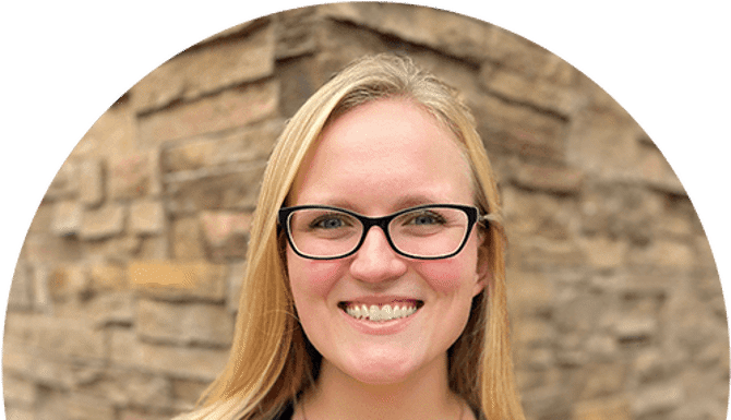 Woman with glasses smiling at camera against brick wall background