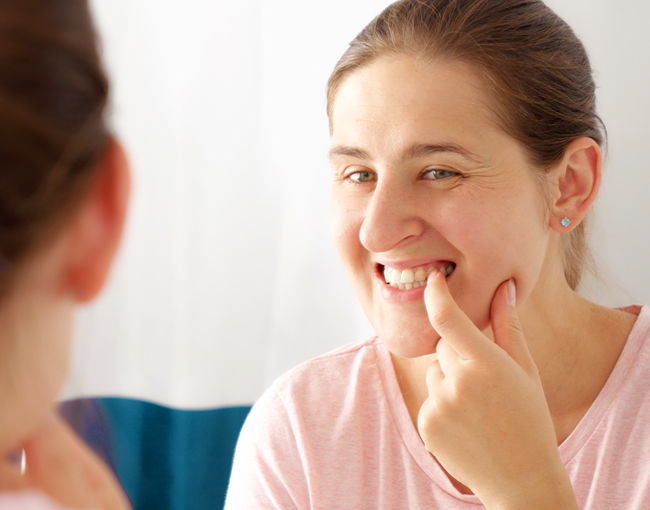 Woman examining her gums and teeth in mirror, dental health self-assessment.