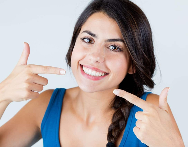 Woman smiling while pointing at her teeth against white background