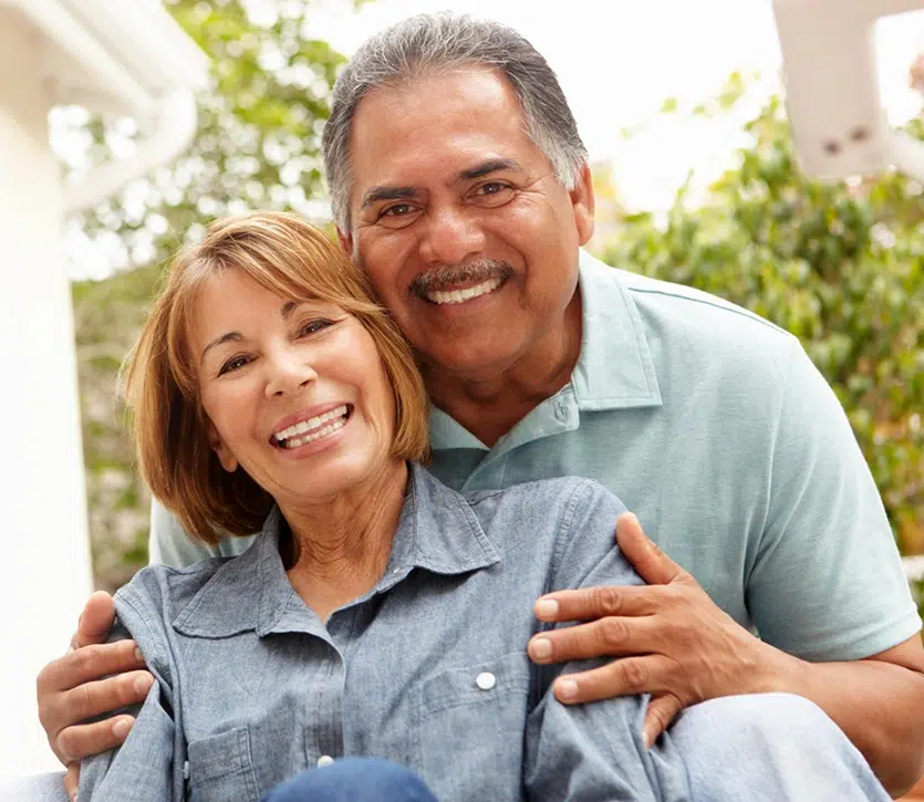 Smiling middle-aged couple embracing outdoors in casual clothing, portraying dental health and wellness.